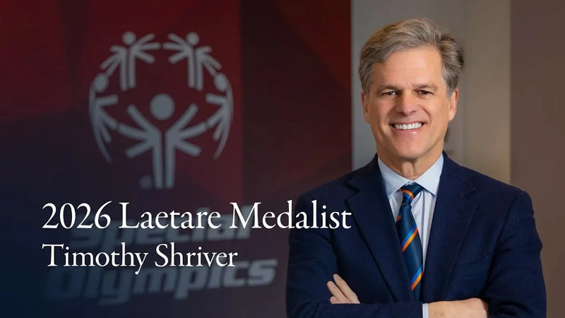 Timothy Shriver, 2026 Laetare Medalist, smiles in a blue suit with a striped tie, arms crossed. Special Olympics logo behind.